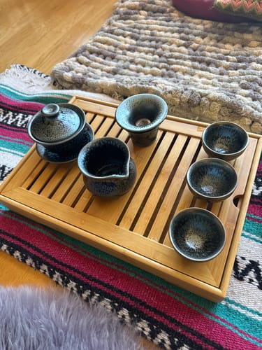 Customer's Glacier Tea Set featuring blue-toned, oil-spot glazed cups and a tea pitcher on a bamboo tray.
